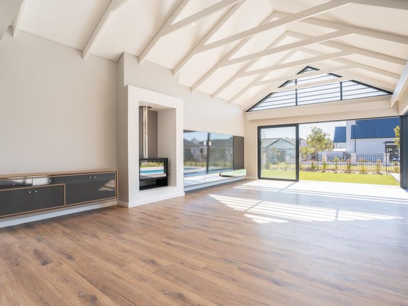 Spacious living area featuring vaulted ceilings with exposed rafters, a modern built-in fireplace, and large sliding glass doors opening to the garden.