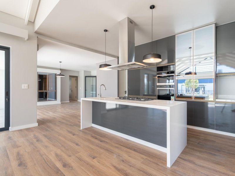 Modern open-plan kitchen featuring a central island with gas hob, integrated appliances, sleek cabinetry, and high-quality laminate flooring in a bright, contemporary space.