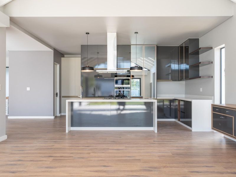 Modern open-plan kitchen featuring high-gloss cabinetry, a central island with integrated hob, built-in oven, and sleek stone countertops.