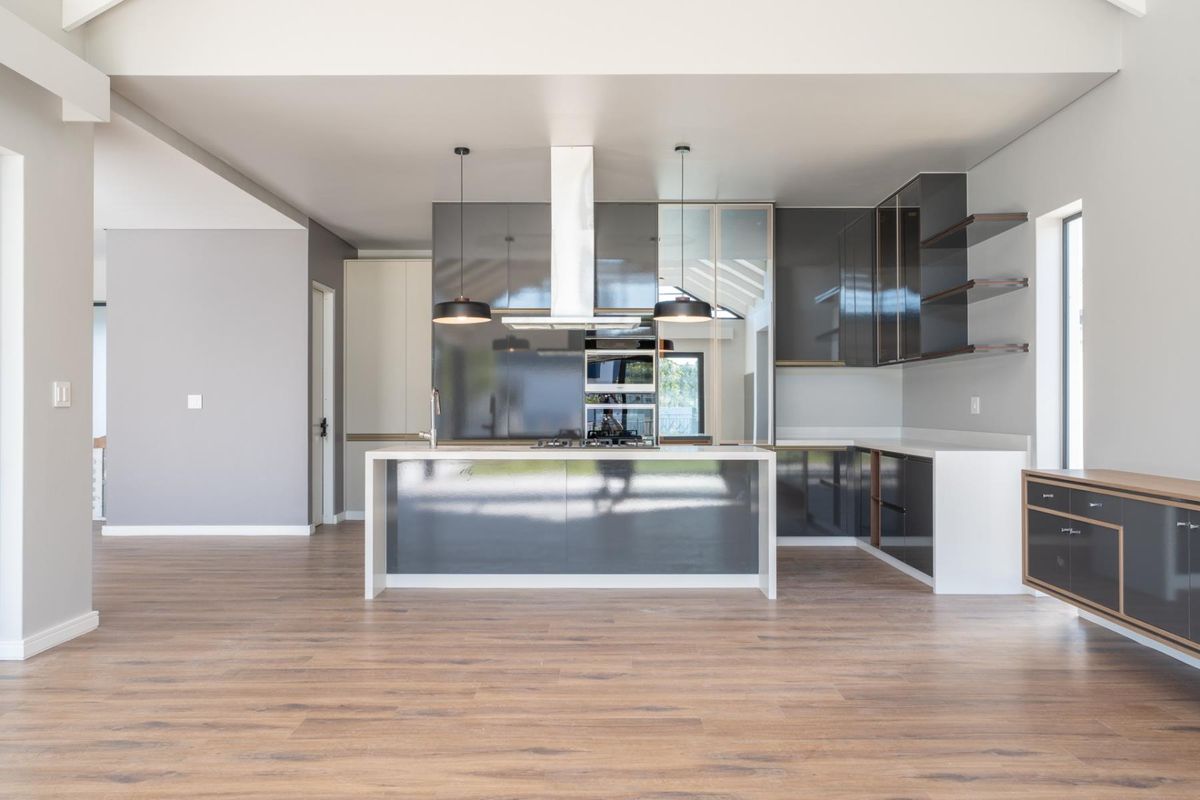 Modern open-plan kitchen featuring high-gloss cabinetry, a central island with integrated hob, built-in oven, and sleek stone countertops.