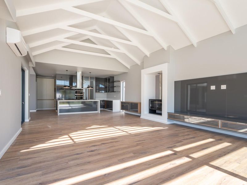 Spacious open-plan living and kitchen area featuring vaulted ceilings with exposed rafters, modern cabinetry, a built-in fireplace, and high-quality wood-look flooring.