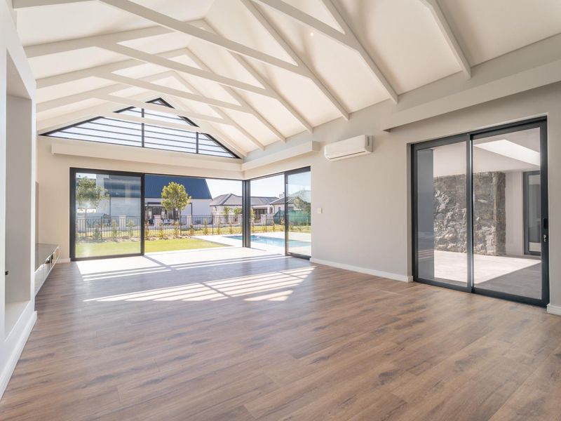 Spacious living area featuring a high vaulted ceiling with exposed rafters, laminate flooring, and large sliding glass doors opening to the pool area.