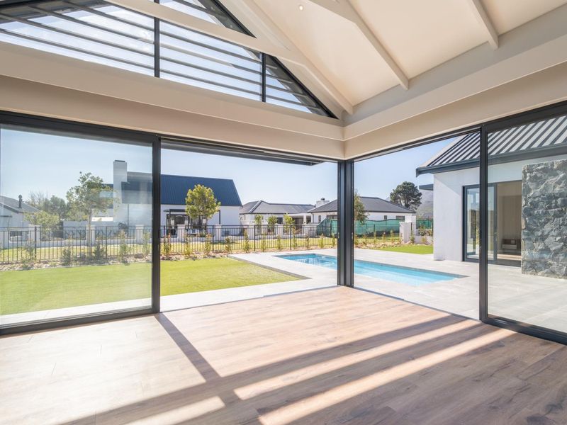 Spacious living area featuring vaulted ceilings, exposed rafters, and expansive sliding glass doors opening onto a private garden and swimming pool.