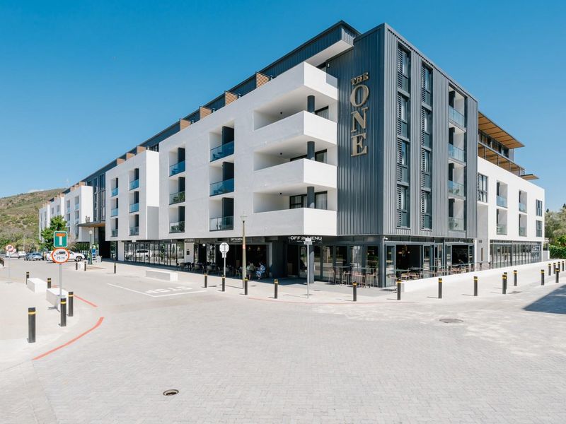Modern multi-story apartment building featuring a contemporary facade, private balconies with glass balustrades, and ground-level commercial space.