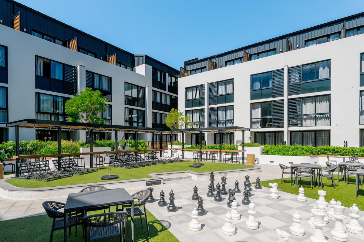 A well-maintained communal courtyard featuring paved areas, artificial turf, pergola structures, and landscaped garden beds within an apartment complex.