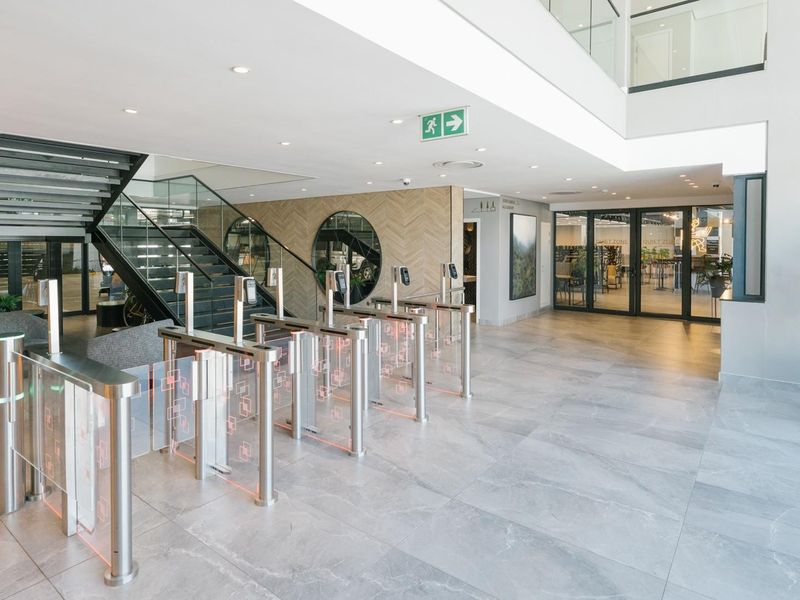 Modern apartment building entrance lobby featuring secure turnstile access, a contemporary glass staircase, and high-quality porcelain tile flooring.