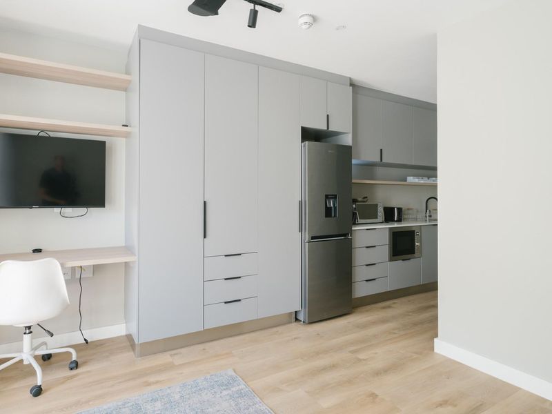 Modern open-plan apartment featuring a sleek kitchen with integrated cabinetry, a built-in workspace with floating shelves, and light wood-look laminate flooring.