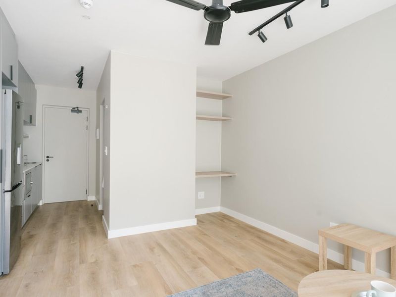 Modern open-plan living area featuring light laminate flooring, built-in cabinetry, integrated shelving, and a ceiling fan in a clean, neutral aesthetic.