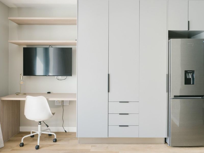 Modern open-plan living area featuring a built-in workspace with shelving, ample storage cabinetry, and a sleek kitchen section with integrated appliances.