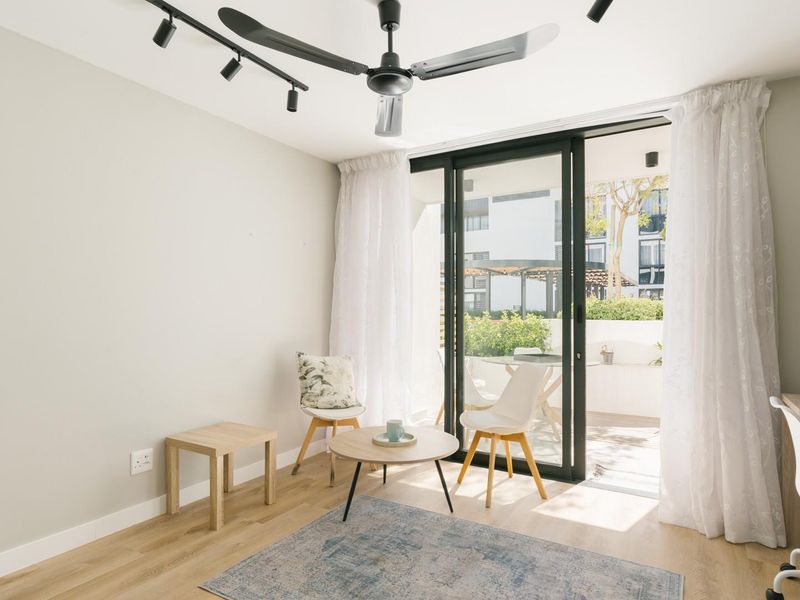Bright living area featuring modern laminate flooring, track lighting, a ceiling fan, and a sliding glass door providing access to a private balcony.