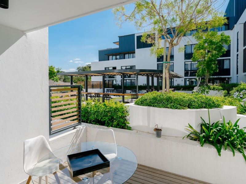 A modern balcony featuring timber decking and a built-in concrete planter, overlooking a landscaped communal courtyard area.