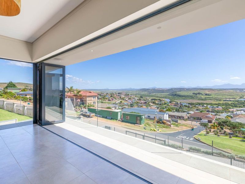 Spacious covered balcony featuring modern tiled flooring, glass balustrades, and wide stacking doors offering expansive elevated views of the surrounding landscape.