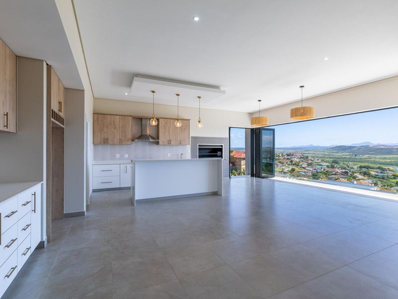 Spacious open-plan kitchen and living area featuring modern cabinetry, a built-in braai, and large stacking doors opening to panoramic landscape views.