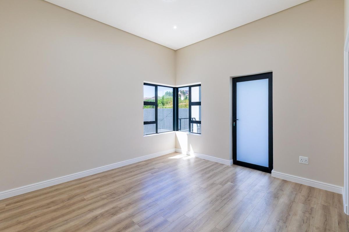A bright, empty bedroom featuring modern laminate flooring, corner windows for natural light, and a sleek frosted glass door leading outside.