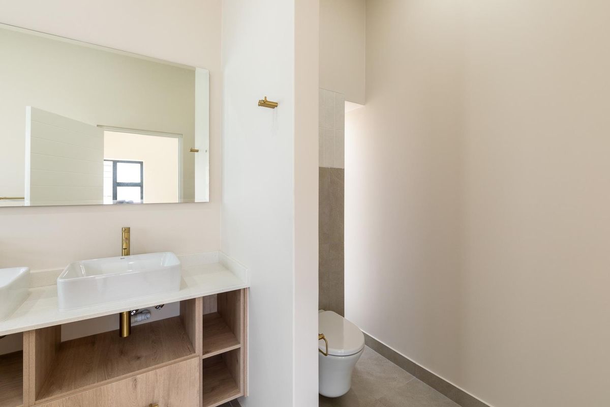 Modern bathroom featuring a double vanity with vessel sinks, brass fixtures, and a separate toilet area with neutral tiling.