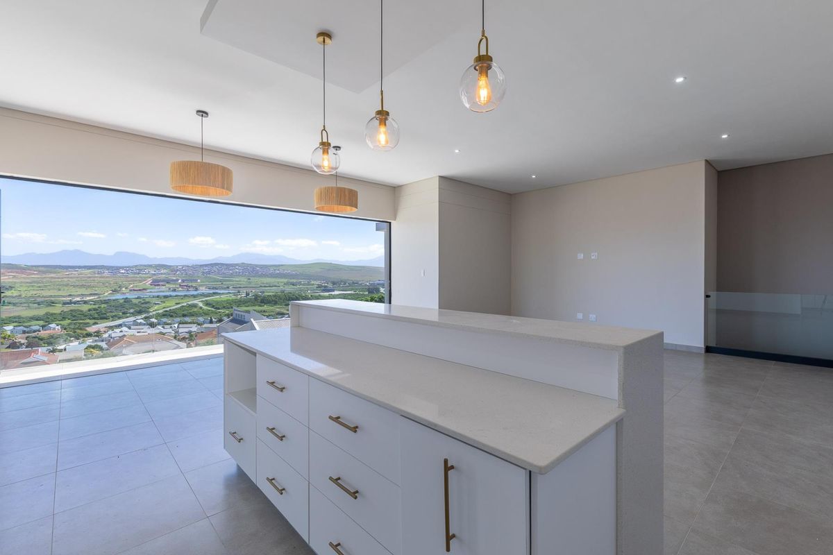 Modern kitchen island with stone countertop and sleek cabinetry, featuring expansive windows with panoramic landscape views and contemporary pendant lighting.
