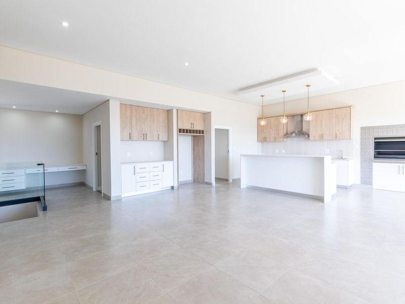 Spacious open-plan living area featuring a modern kitchen with built-in cabinetry, a central island, and a built-in braai, finished with neutral floor tiles.