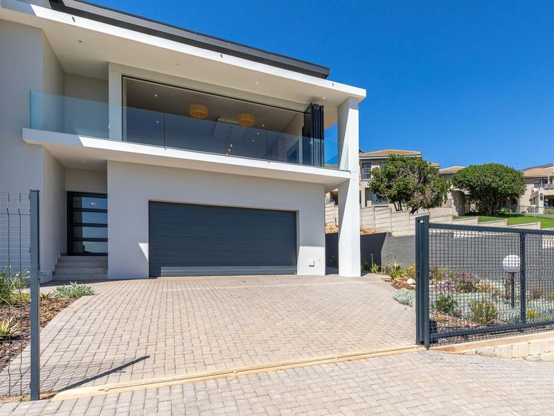Modern double-storey home featuring a paved driveway, secure garage, and a spacious covered balcony with glass balustrades.