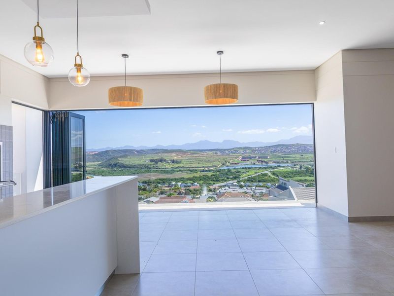 Spacious open-plan living area featuring a built-in fireplace, stone breakfast bar, and large stacking doors opening to expansive panoramic mountain and valley views.