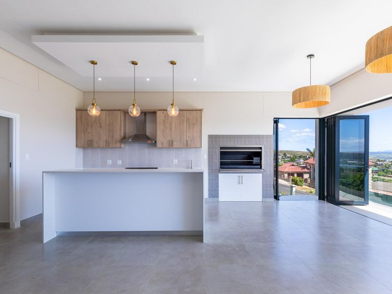 Modern open-plan living area featuring a sleek kitchen island, built-in braai, and large stacking doors opening to a scenic view.