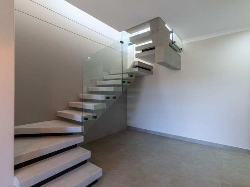 Modern entrance hallway featuring a striking floating concrete staircase with a sleek glass balustrade and neutral tiled flooring.