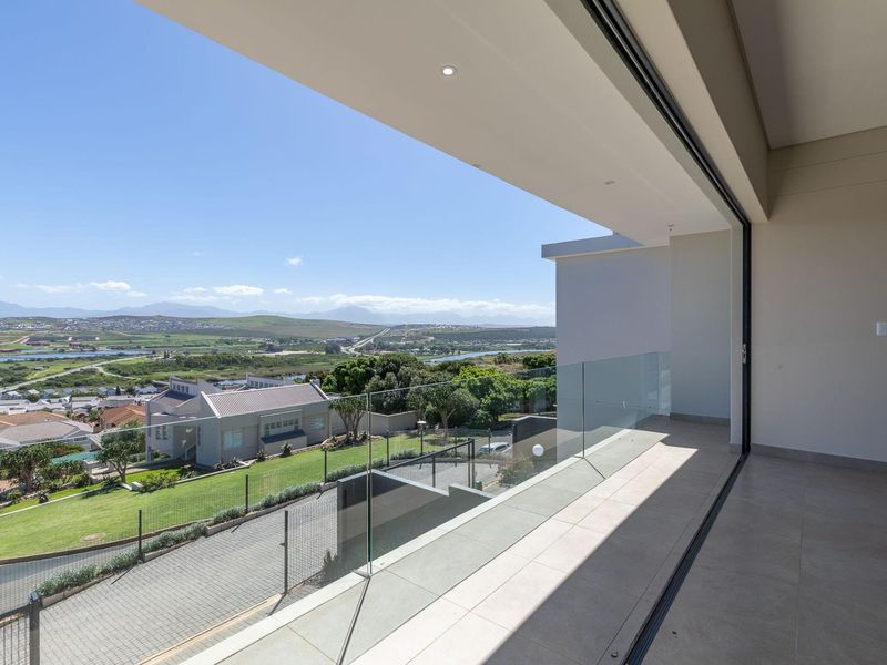 A modern covered balcony featuring a frameless glass balustrade and expansive views over the surrounding residential estate and landscape.