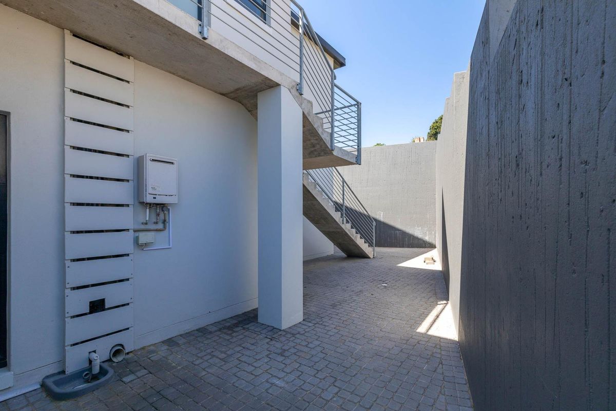 A modern rear courtyard featuring a concrete staircase with metal railings, paved flooring, and a wall-mounted gas geyser unit.