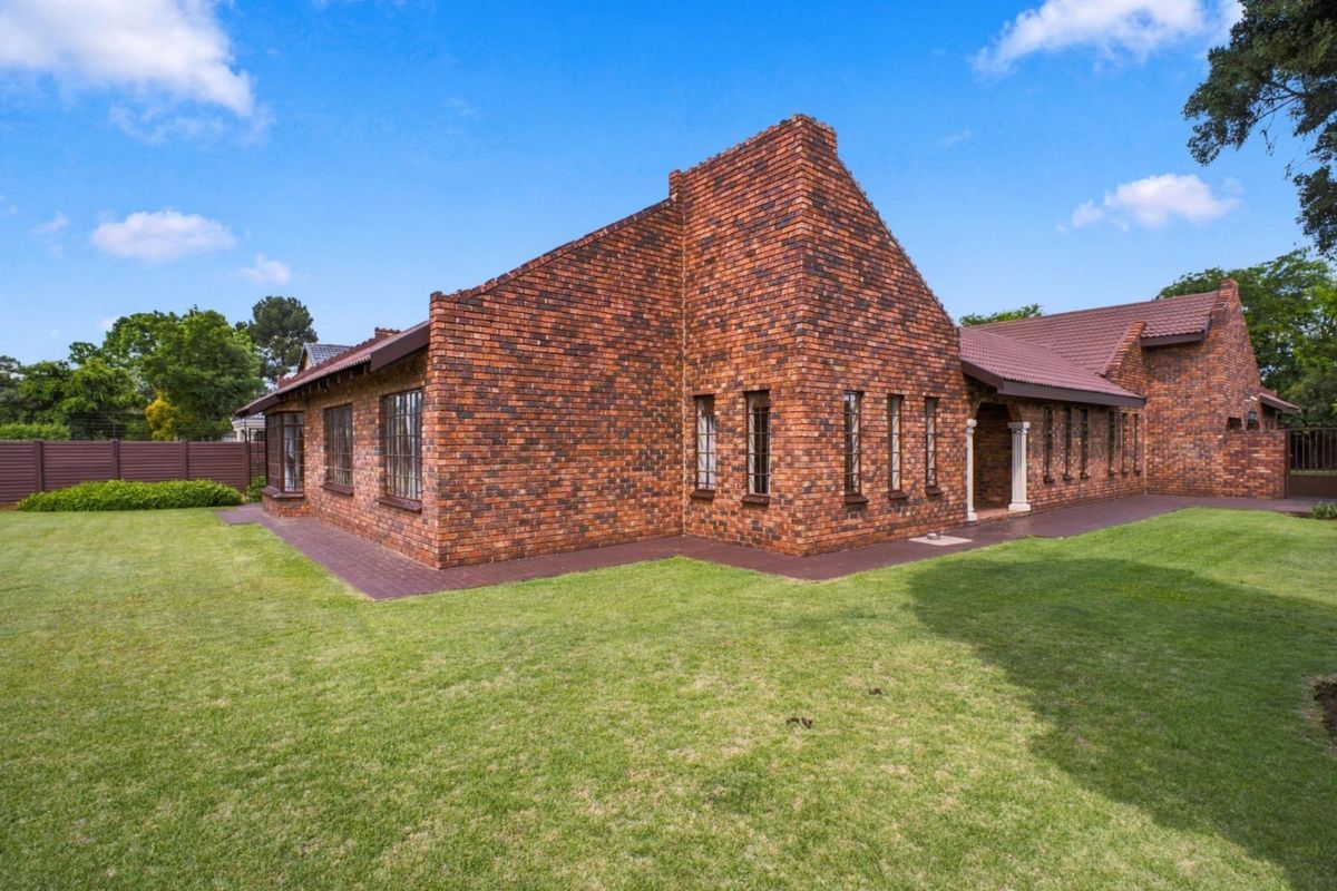 A well-maintained face brick house exterior featuring a tiled roof, paved walkways, and a spacious surrounding lawn.