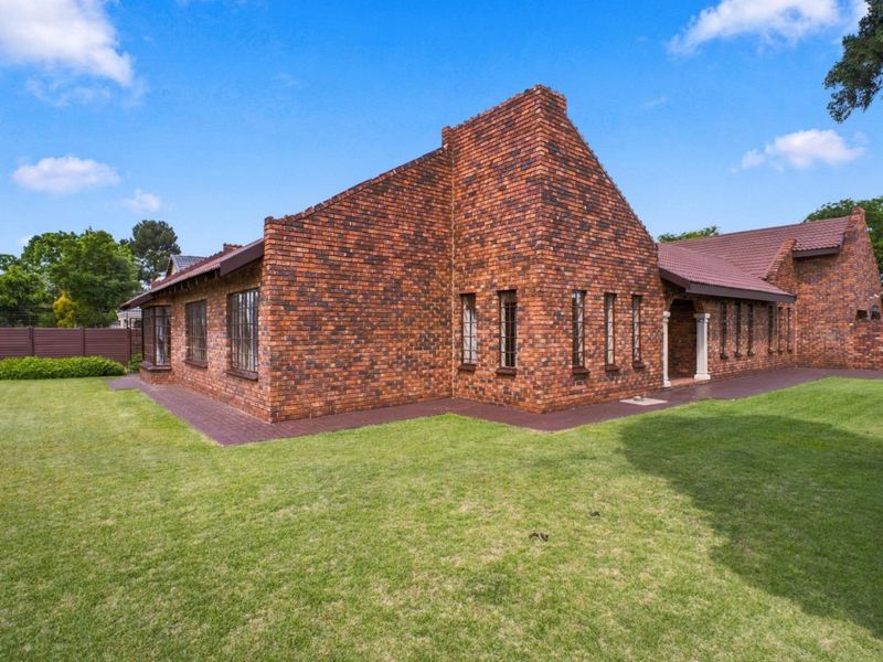 A well-maintained face brick house exterior featuring a tiled roof, paved walkways, and a spacious surrounding lawn.