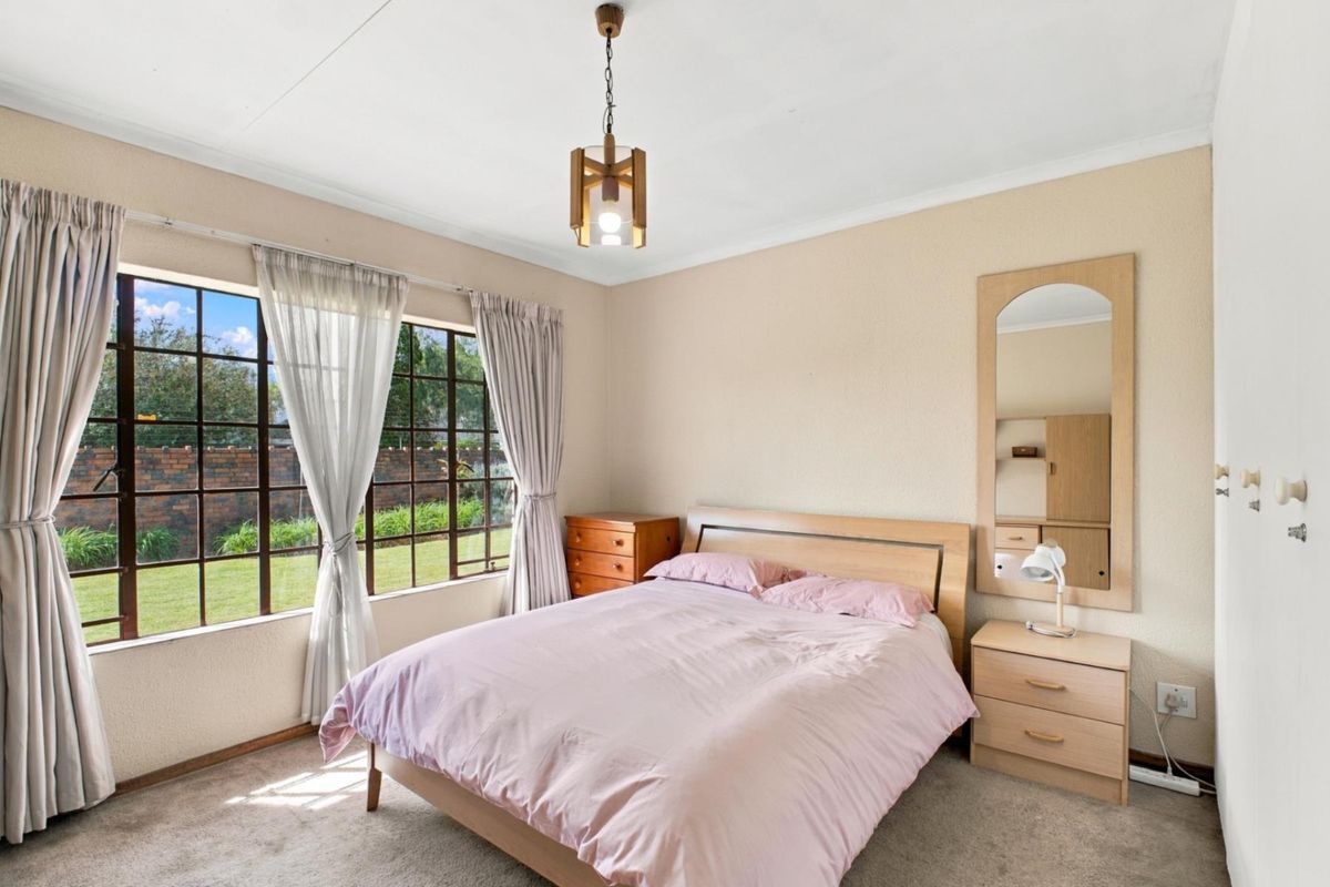 A well-lit bedroom featuring large windows, carpeted flooring, and built-in wardrobe storage, offering a comfortable and functional living space.