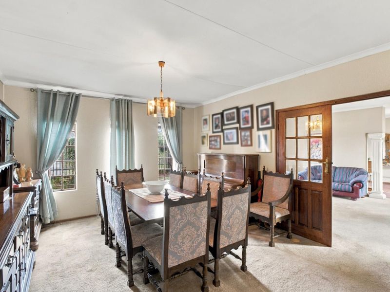 A traditional dining room featuring carpeted flooring, a coved ceiling, and a timber-framed glass door leading to an adjacent living area.