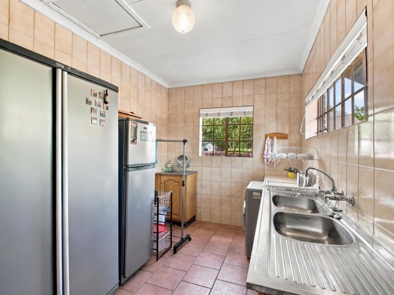 A functional scullery area featuring tiled walls, tiled flooring, and a double stainless steel sink with integrated drainer.