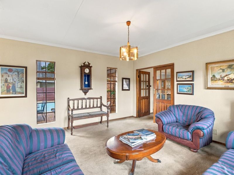 A traditional living room featuring carpeted flooring, vertical windows, and a timber-framed glass door leading to adjacent spaces.