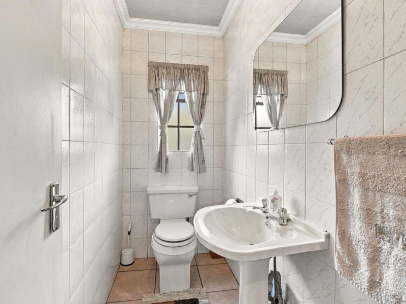 A compact guest bathroom featuring full-height wall tiling, a pedestal sink, and a standard toilet.