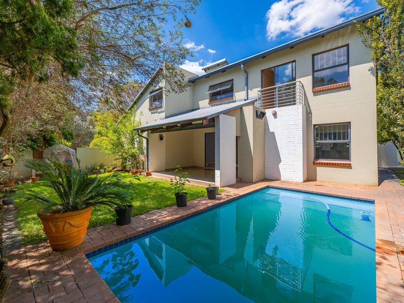 Rear view of the townhouse featuring a swimming pool, brick-paved surround, covered patio area, and an upper-level balcony with metal railings.