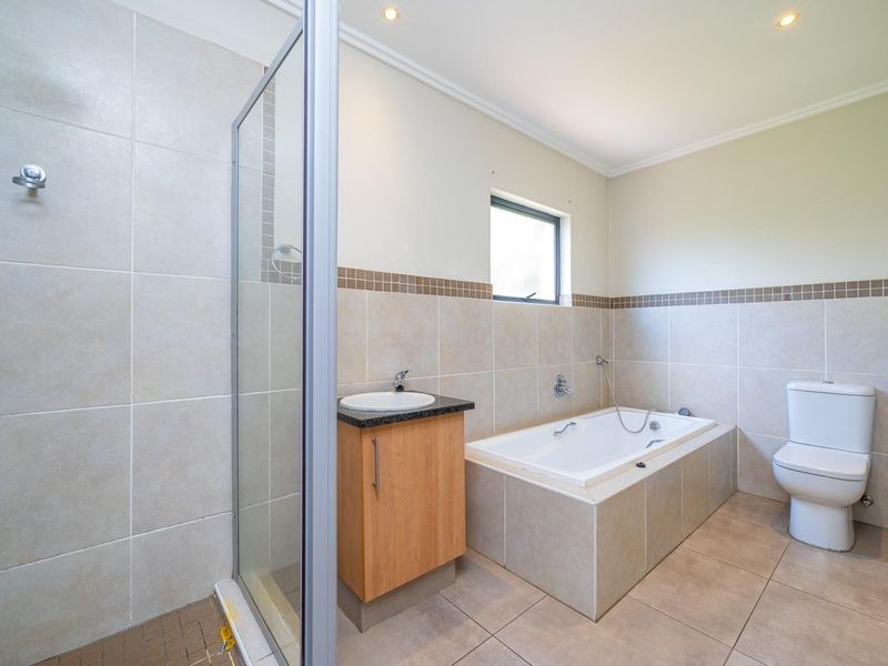 A clean, functional bathroom featuring a separate shower enclosure, a built-in bathtub, a vanity unit with a basin, and neutral floor-to-ceiling wall tiling.