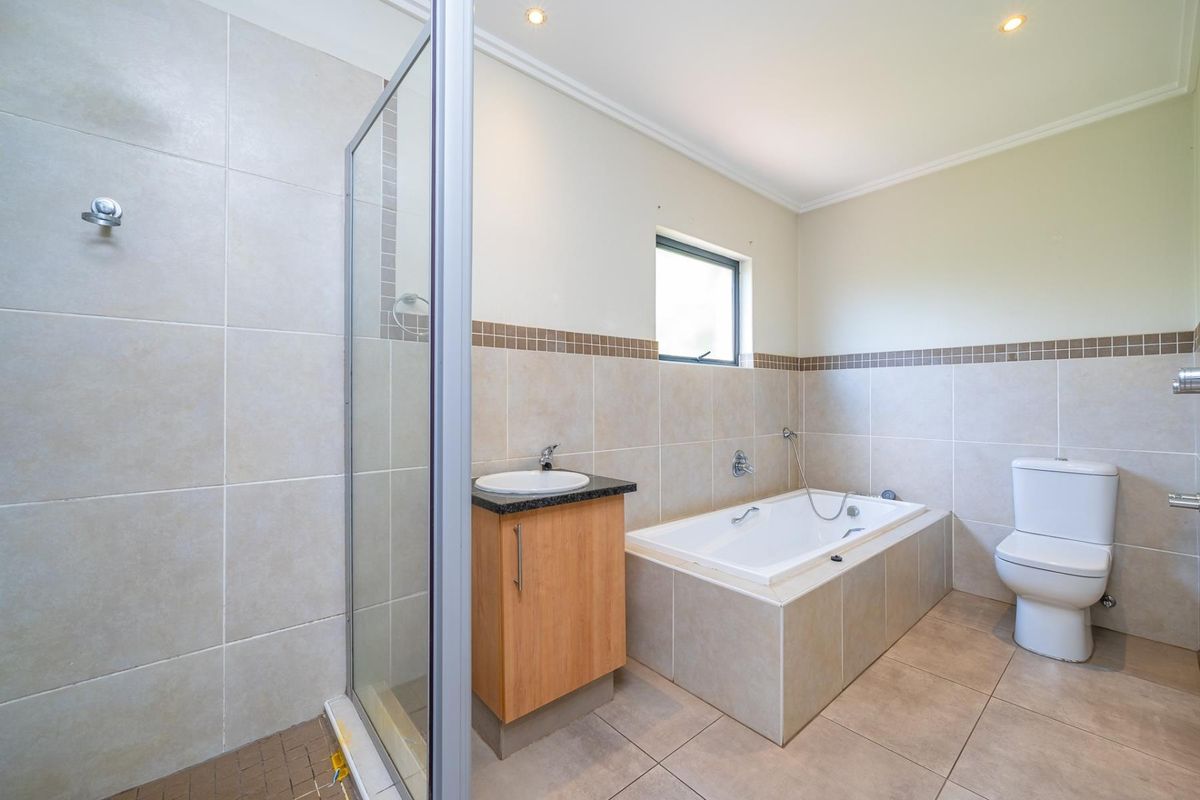 A clean, functional bathroom featuring a separate shower enclosure, a built-in bathtub, a vanity unit with a basin, and neutral floor-to-ceiling wall tiling.