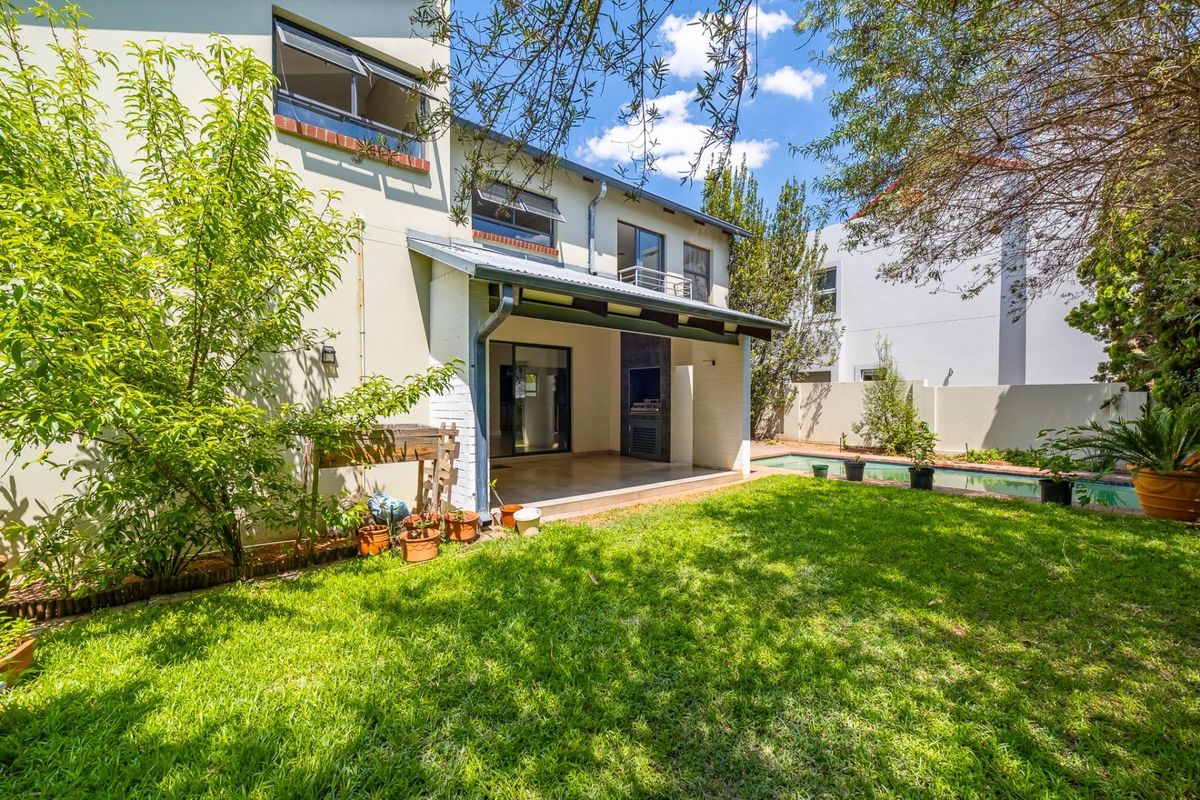 Rear view of the townhouse featuring a covered patio with a built-in braai, a private garden, and a swimming pool.