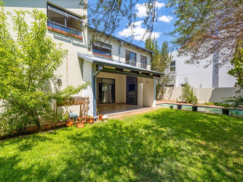 Rear view of the townhouse featuring a covered patio with a built-in braai, a private garden, and a swimming pool.