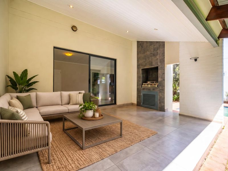A covered patio area featuring tiled flooring, a built-in braai, and direct access to the garden and pool area through sliding glass doors.