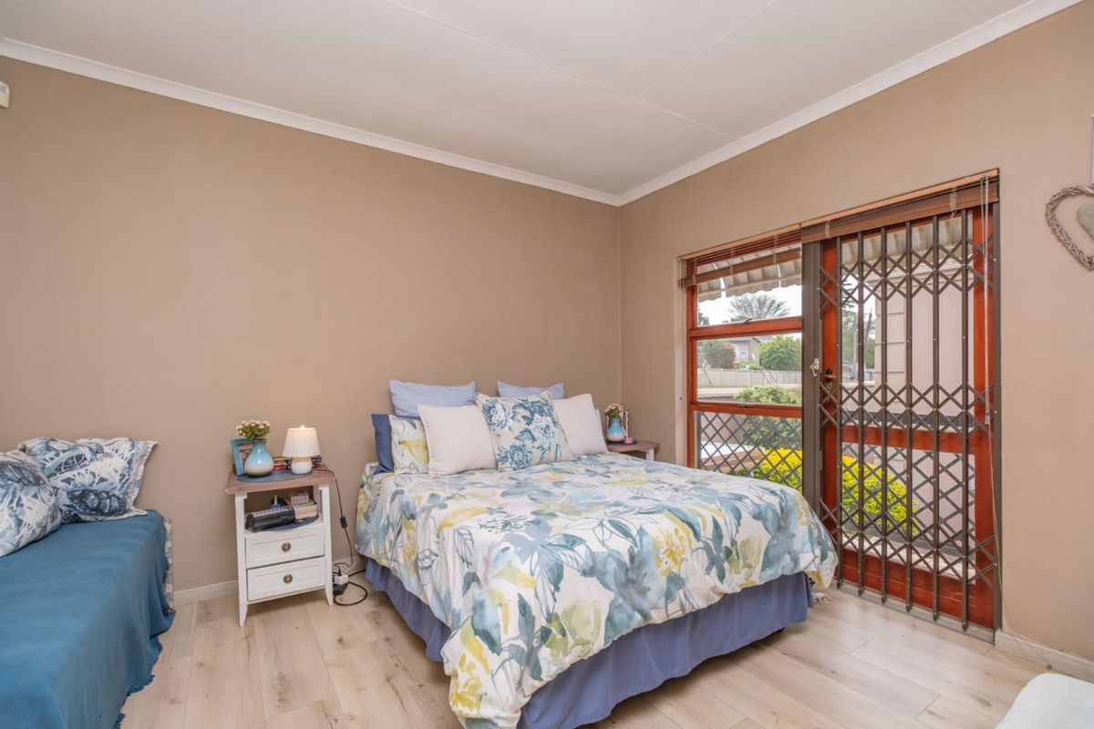 A bedroom featuring light-toned laminate flooring, neutral wall paint, and a sliding glass door with an integrated security gate providing access to the exterior.