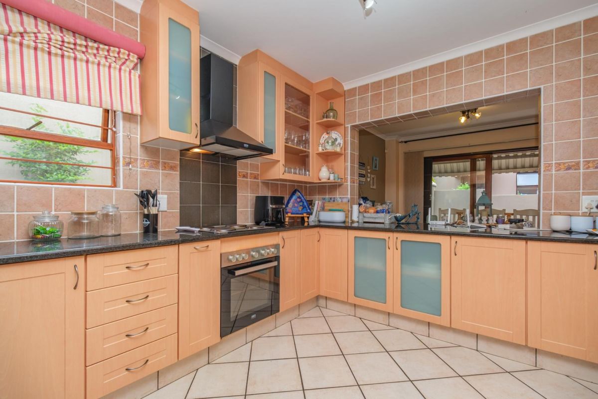 A functional kitchen featuring light wood cabinetry, granite countertops, ceramic tile backsplash, and built-in appliances, with an open-plan layout connecting to the living area.