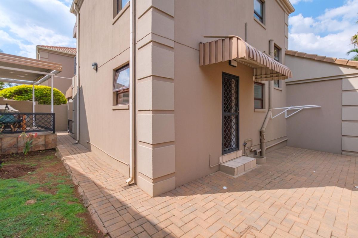 Rear exterior view of the townhouse featuring a paved courtyard, security gate, and functional wall-mounted washing line.