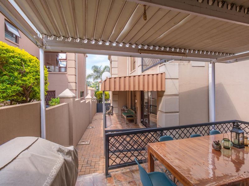 A covered outdoor patio area featuring paved flooring, a metal balustrade, and an awning, providing a functional space for outdoor dining and relaxation.