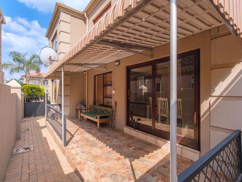 A covered patio area featuring tiled flooring, a retractable awning, and sliding glass door access to the interior of the townhouse.