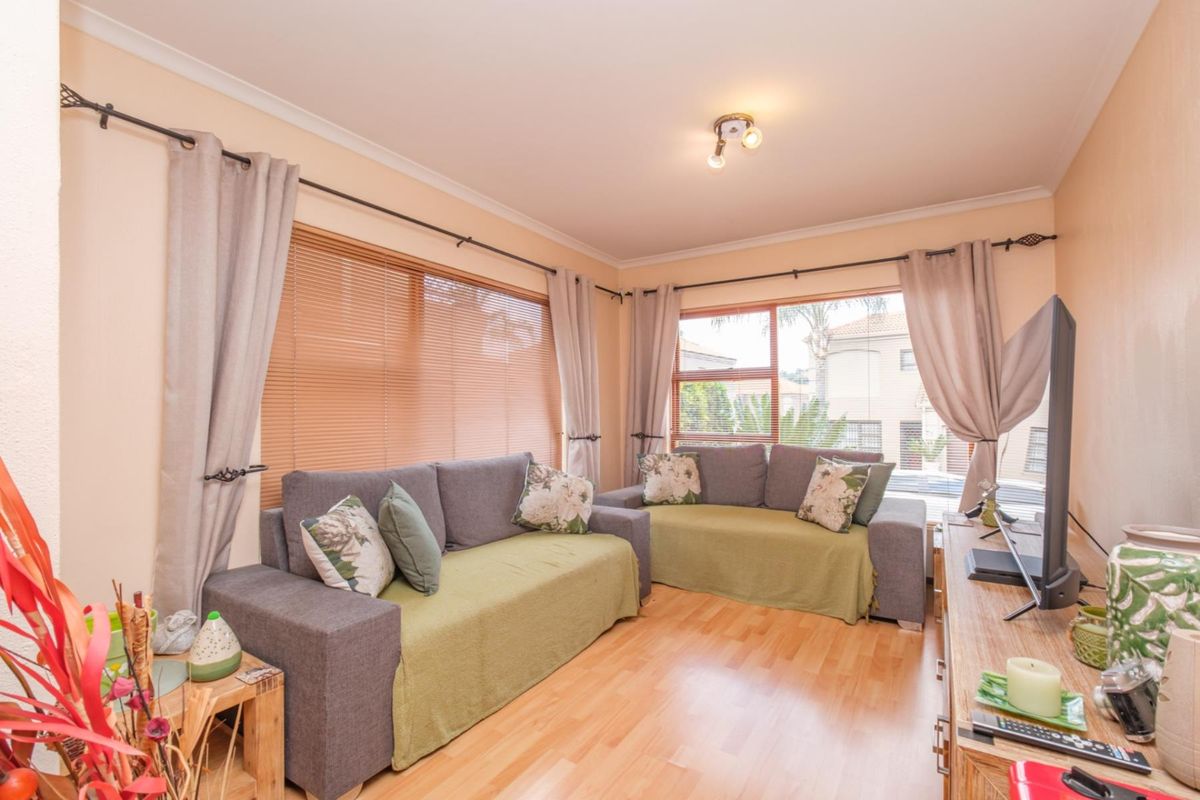 A comfortable living room featuring laminate flooring, large windows with venetian blinds, and neutral wall finishes, providing a bright and functional space.