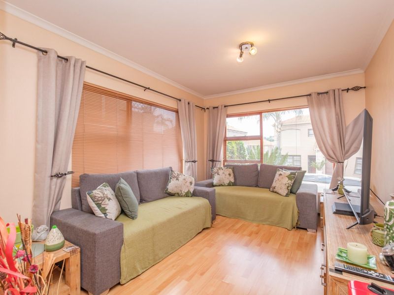 A comfortable living room featuring laminate flooring, large windows with venetian blinds, and neutral wall finishes, providing a bright and functional space.