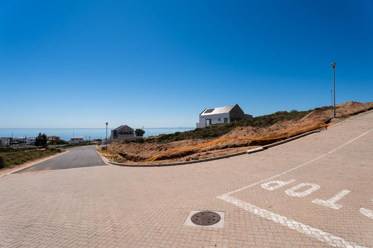 A view of a residential street with paved surfaces, infrastructure, and a vacant plot overlooking the ocean in a coastal development.