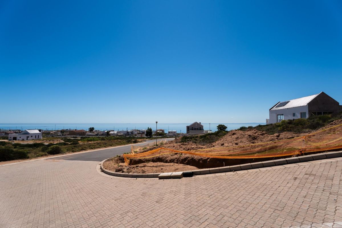 A vacant residential plot featuring paved driveway access, concrete curbing, and expansive coastal views in a developing neighborhood.