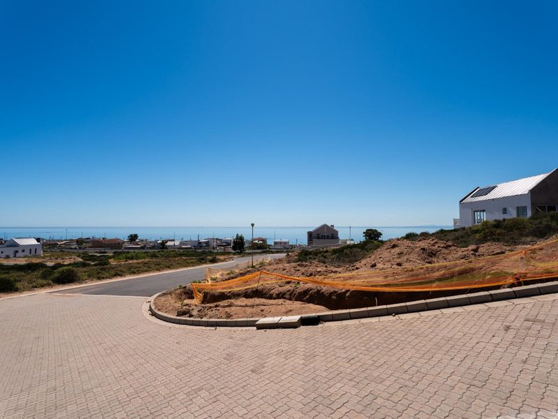 A vacant residential plot featuring paved driveway access, concrete curbing, and expansive coastal views in a developing neighborhood.